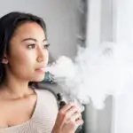 Casual asian woman vaping electronic cigarette at home